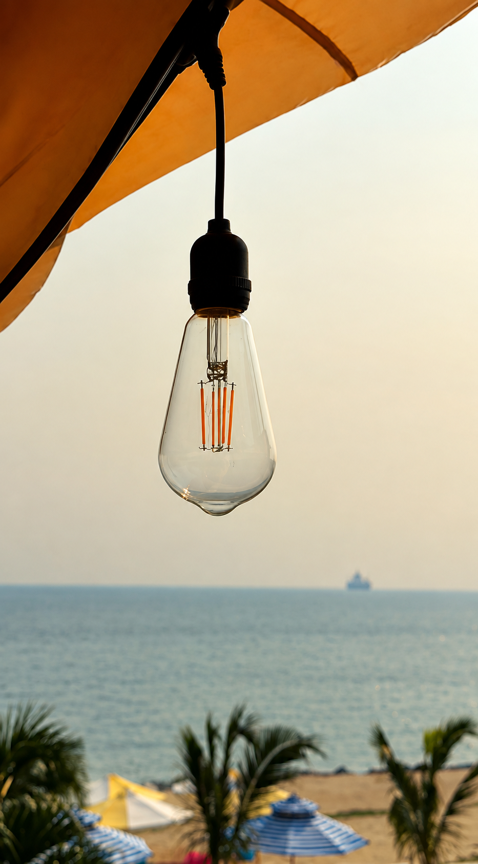 A hanging light bulb beneath an orange parasol, with the sea in the background at MUSE.