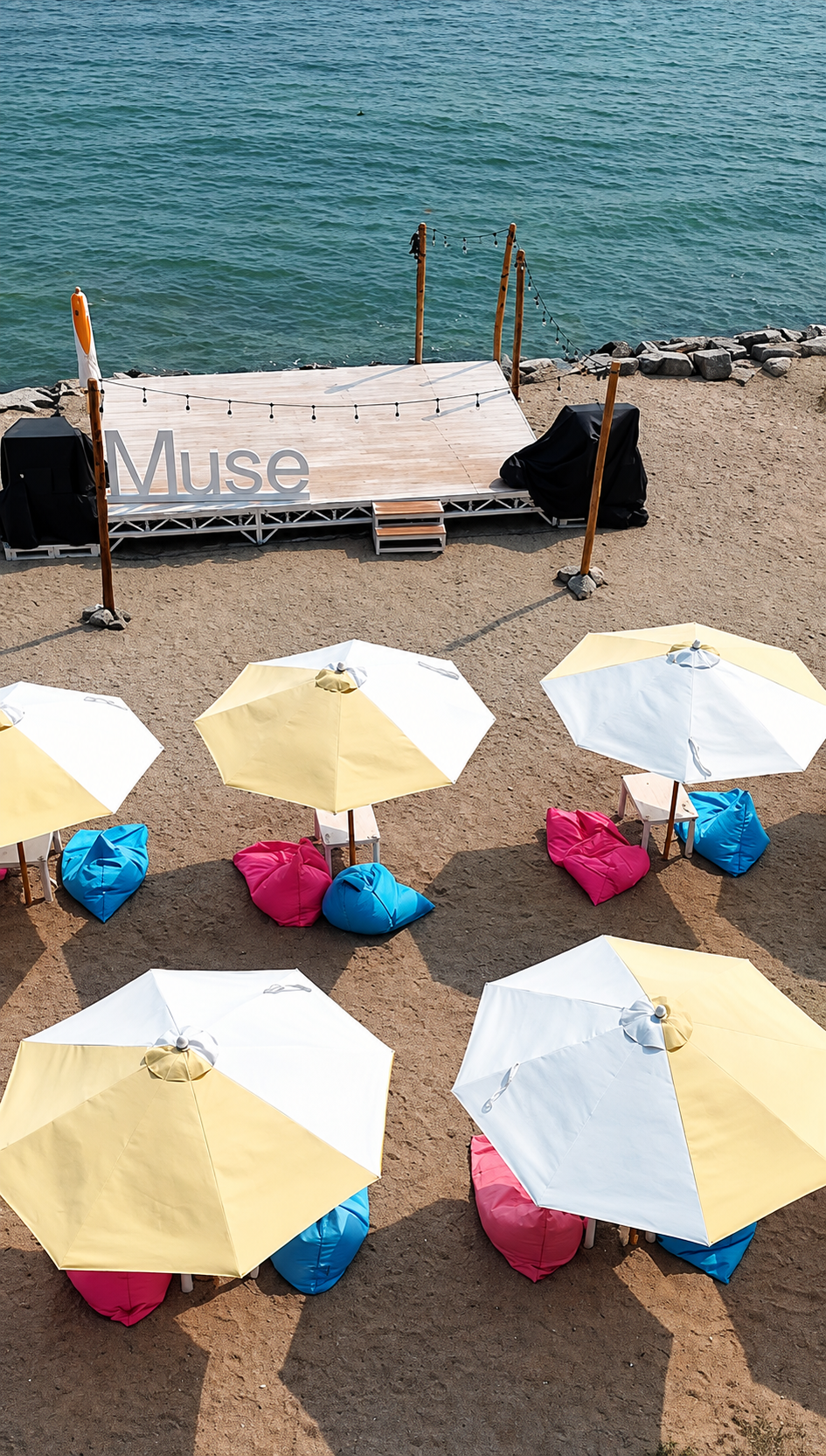 Alt text: Aerial view of MUSE’s seaside seating area, with parasols and colourful beanbags beside the water.